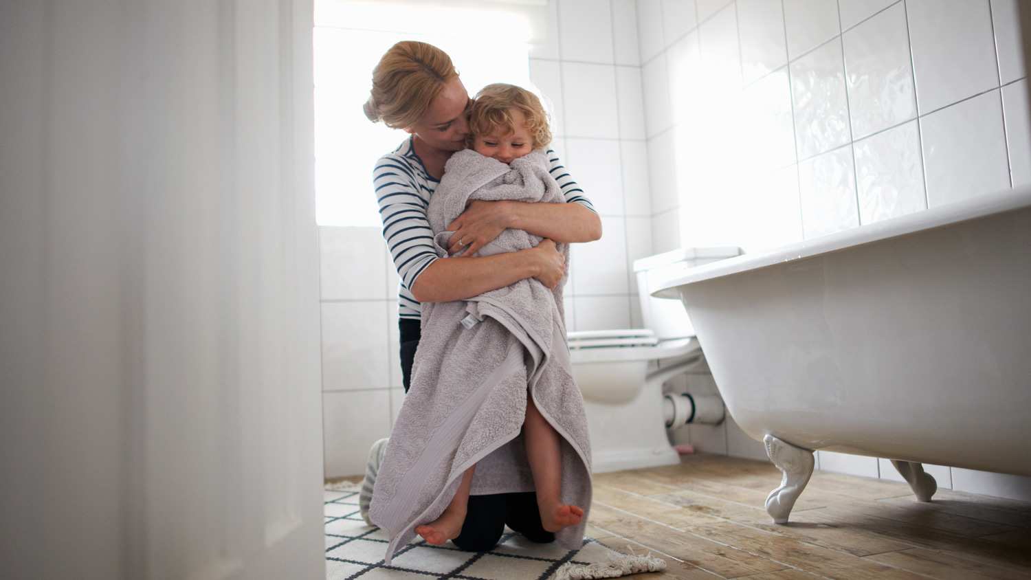 A mother in a bathroom wrapping her daughter with a towel