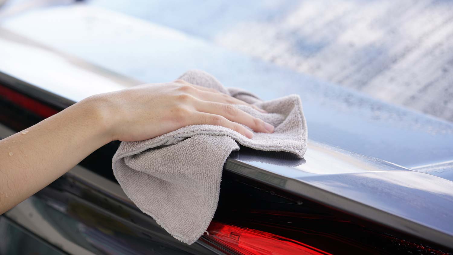 A woman cleaning the car’s exterior with a microfiber cloth