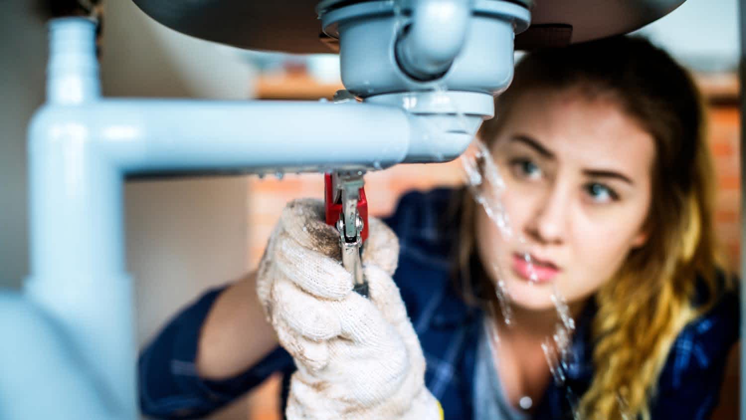 A woman fixing a leaking pipe