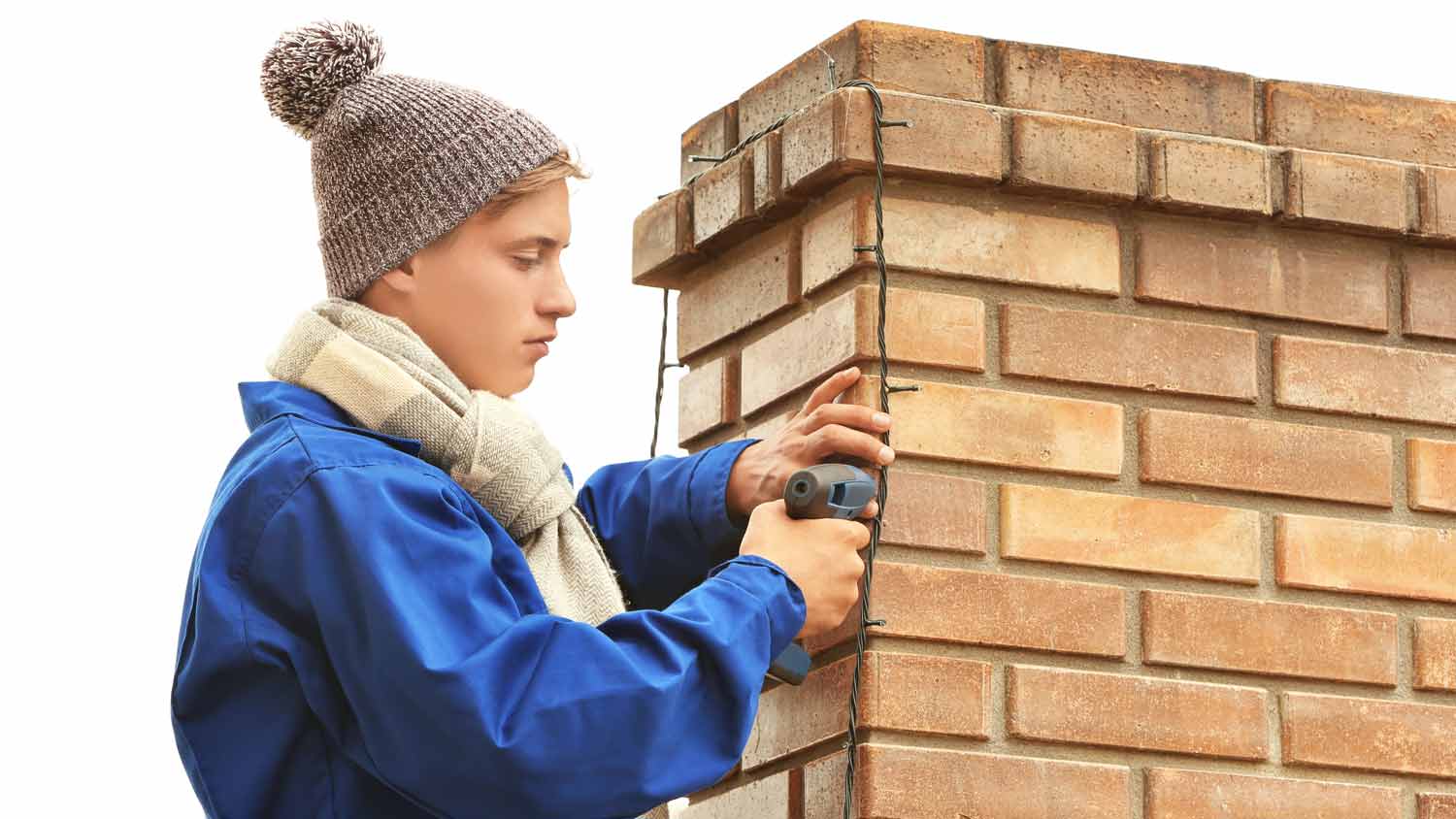 A young man hanging Christmas lights in chimney by using a glue gun