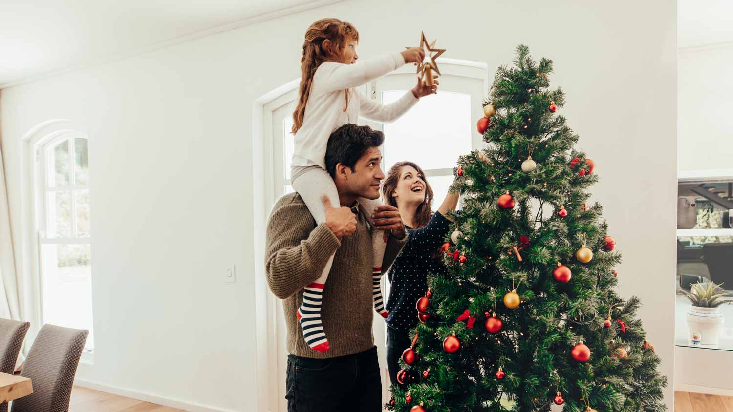 A family of three decorating a Christmas tree