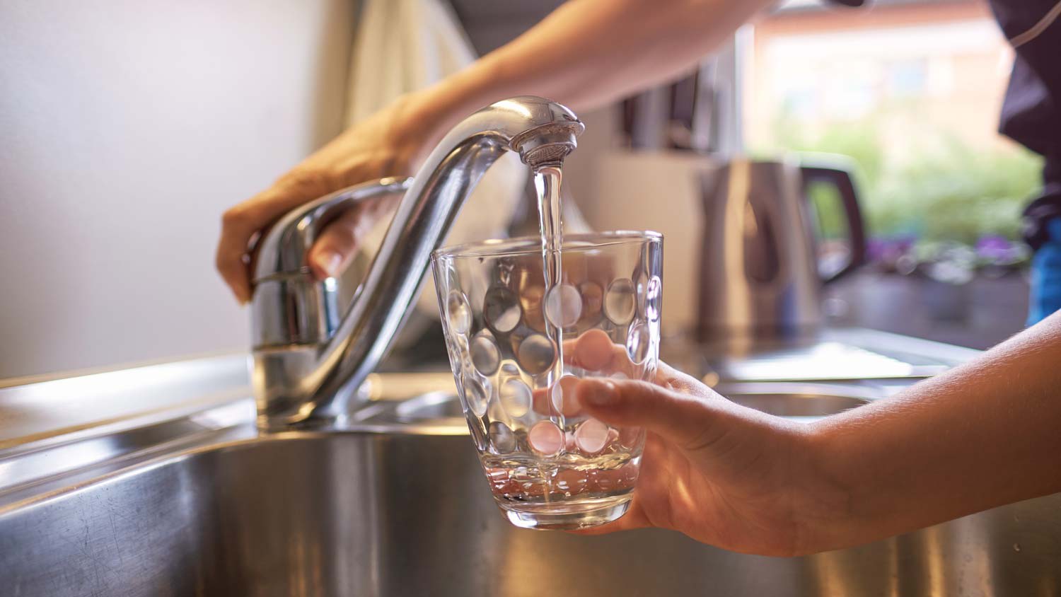 Close-up of a woman and a kid’s hands while filling a glass with tap water