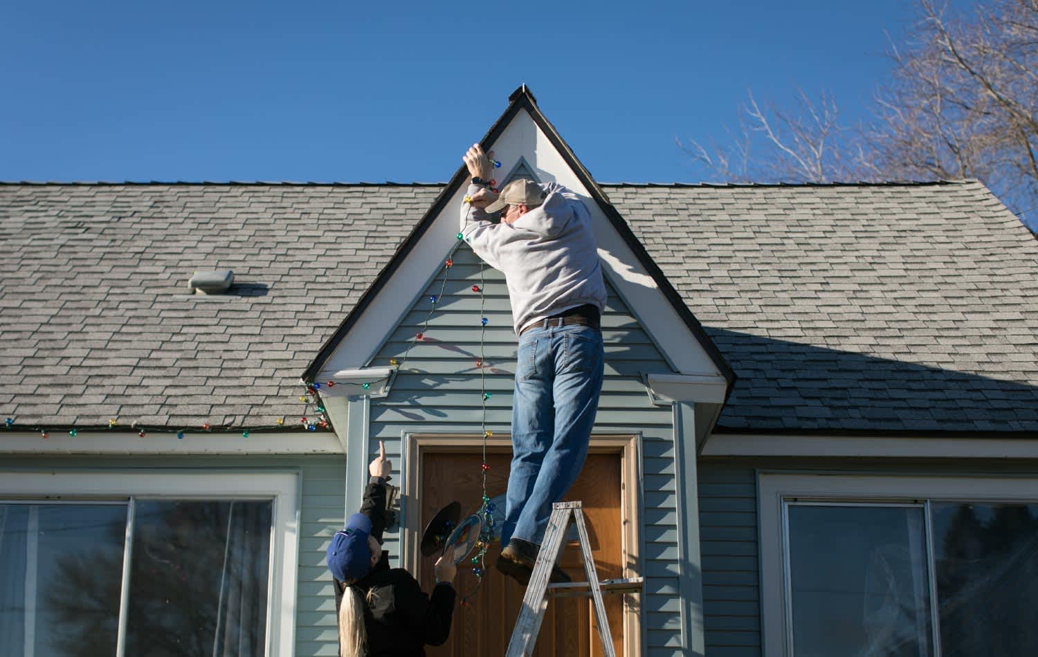 A man hanging Christmas lights on peak of a house