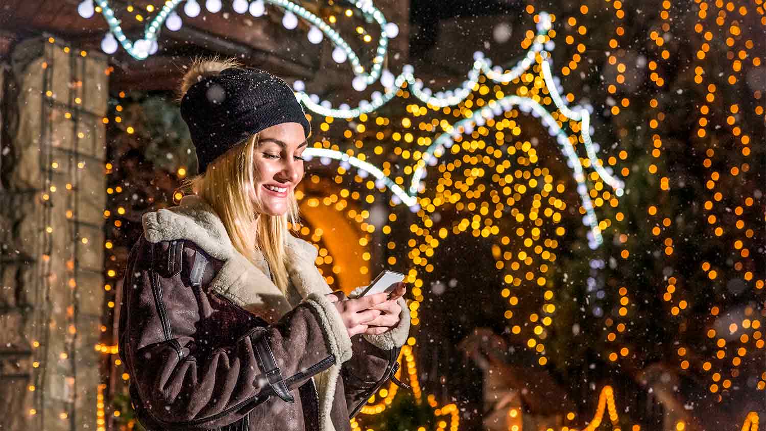 A woman looks at her smartphone in front of Christmas lights