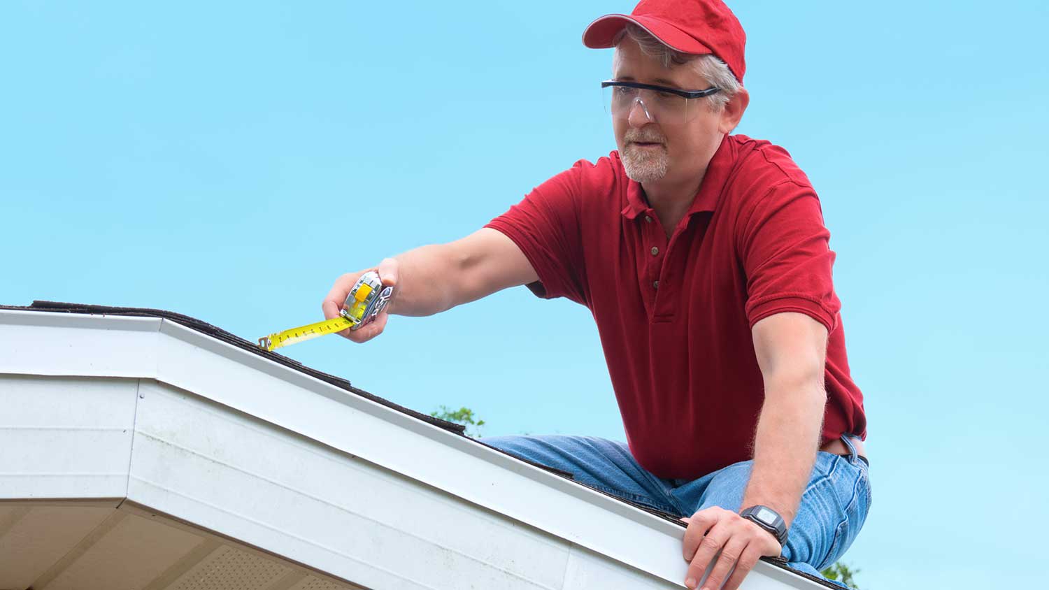 Handyman on a house roof using a measuring tape