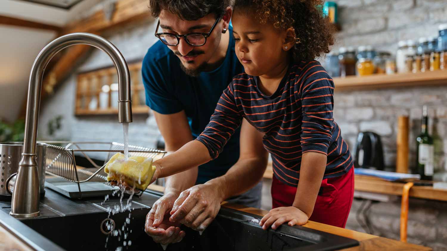 A father with his daughter washing dishes in the sink