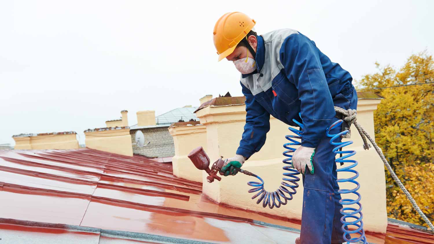 A professional wearing protective gear spray painting a roof