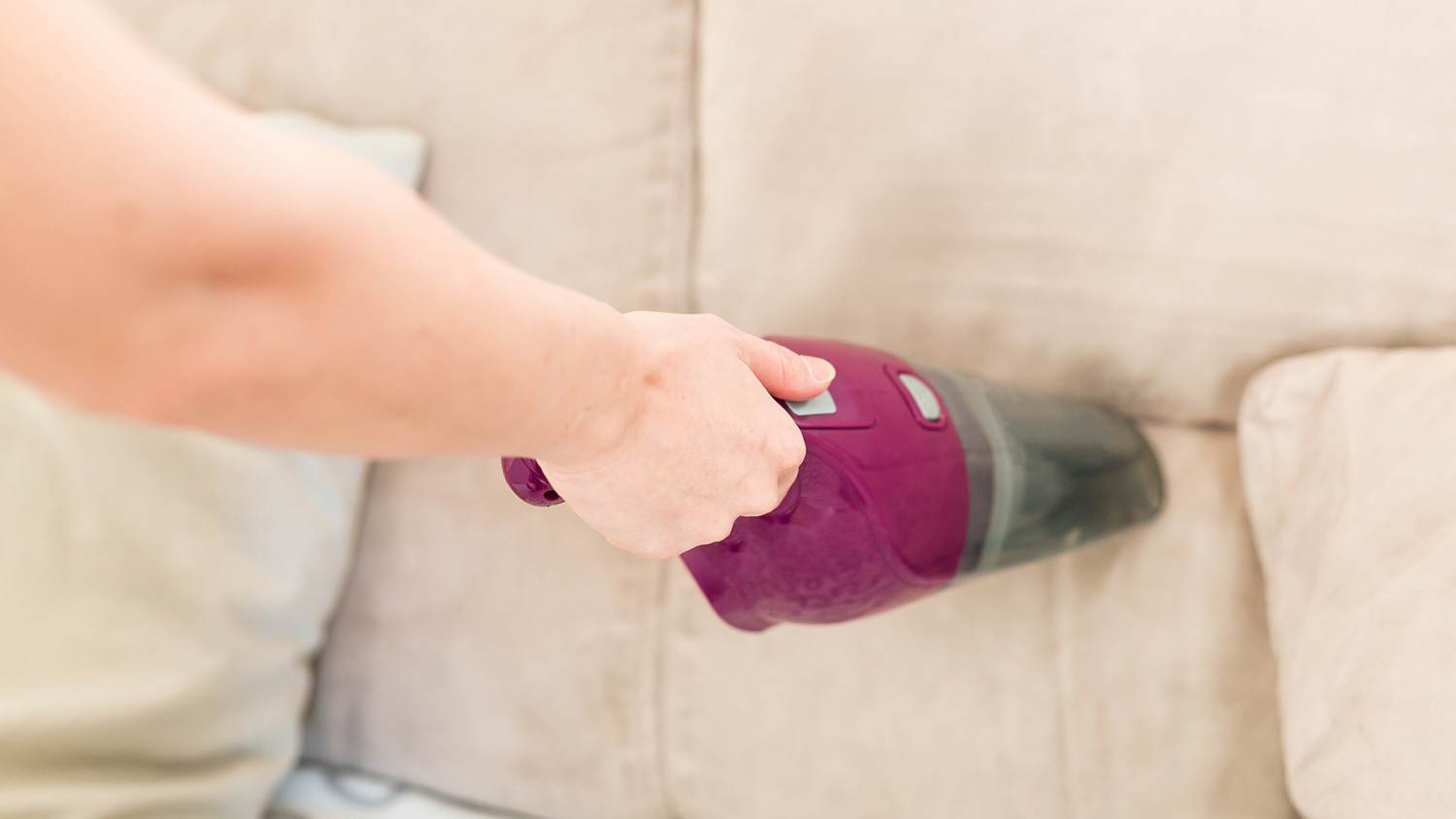 A woman cleaning a couch with a vacuum cleaner