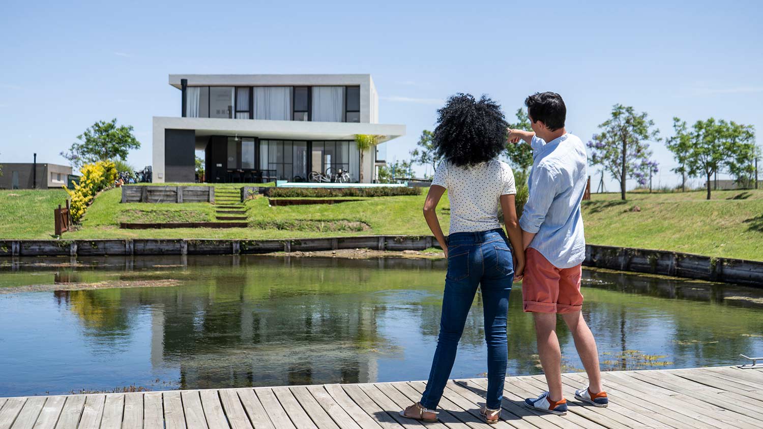 Rear view of couple looking at house while standing on pier by lake