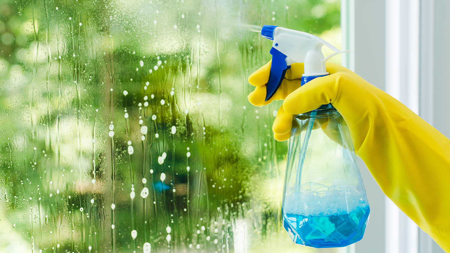 A person sprays glass cleaner on a window