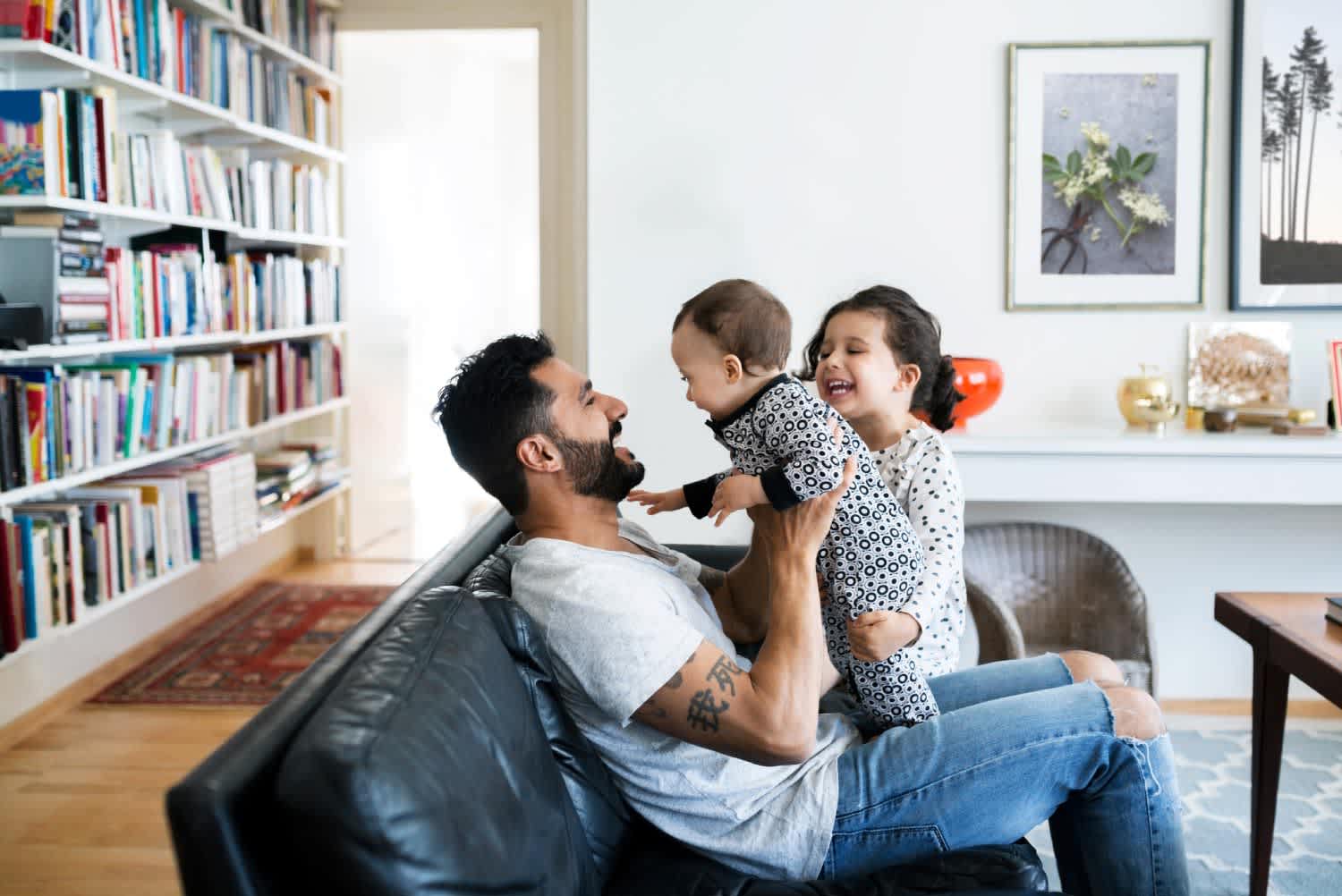 Father and daughter playing with baby girl on sofa at home