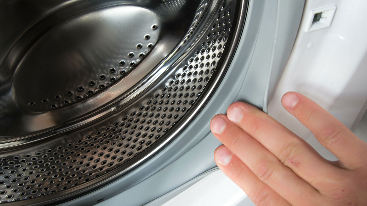 A hand touches the rubber seal on a washing machine