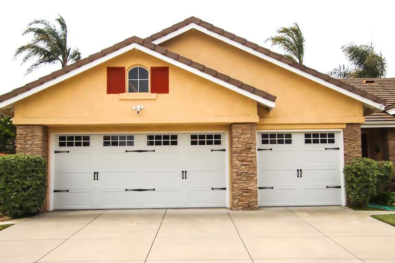 forward view of yellow and brick house with double and single garage and concrete driveway