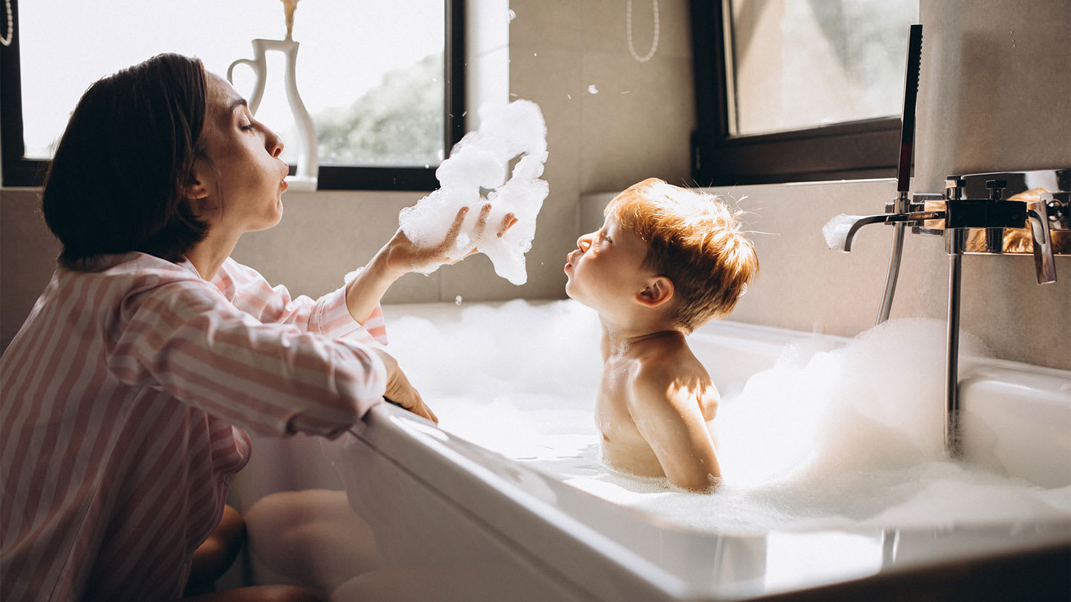 A mother bathes her son in a bathtub
