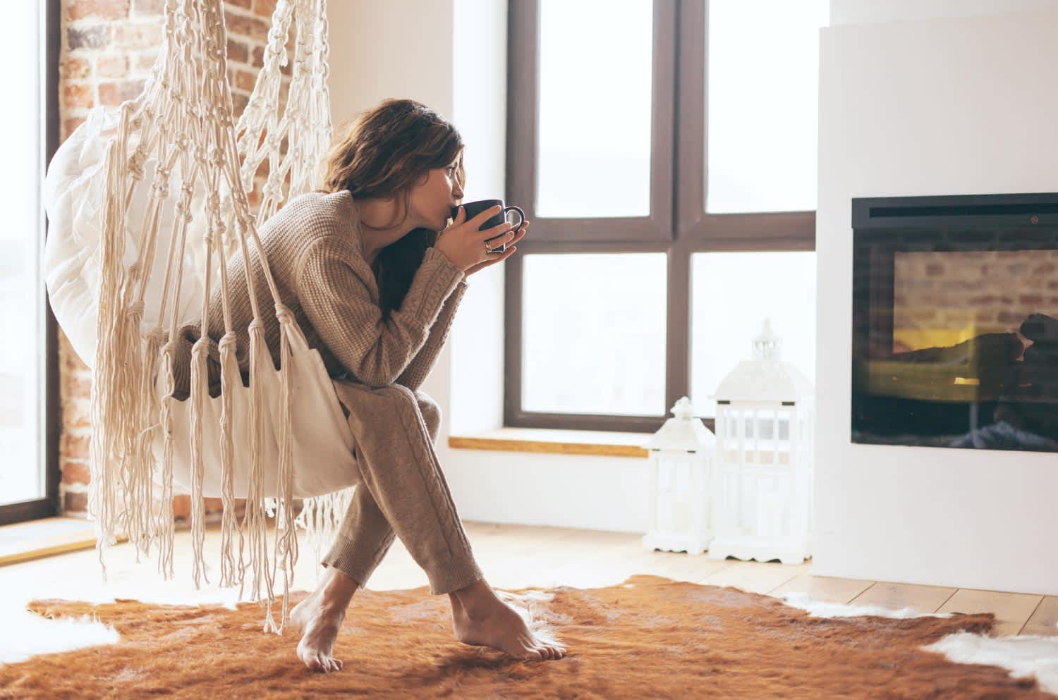 Woman enjoys coffee fireside while sitting in a swinging chair