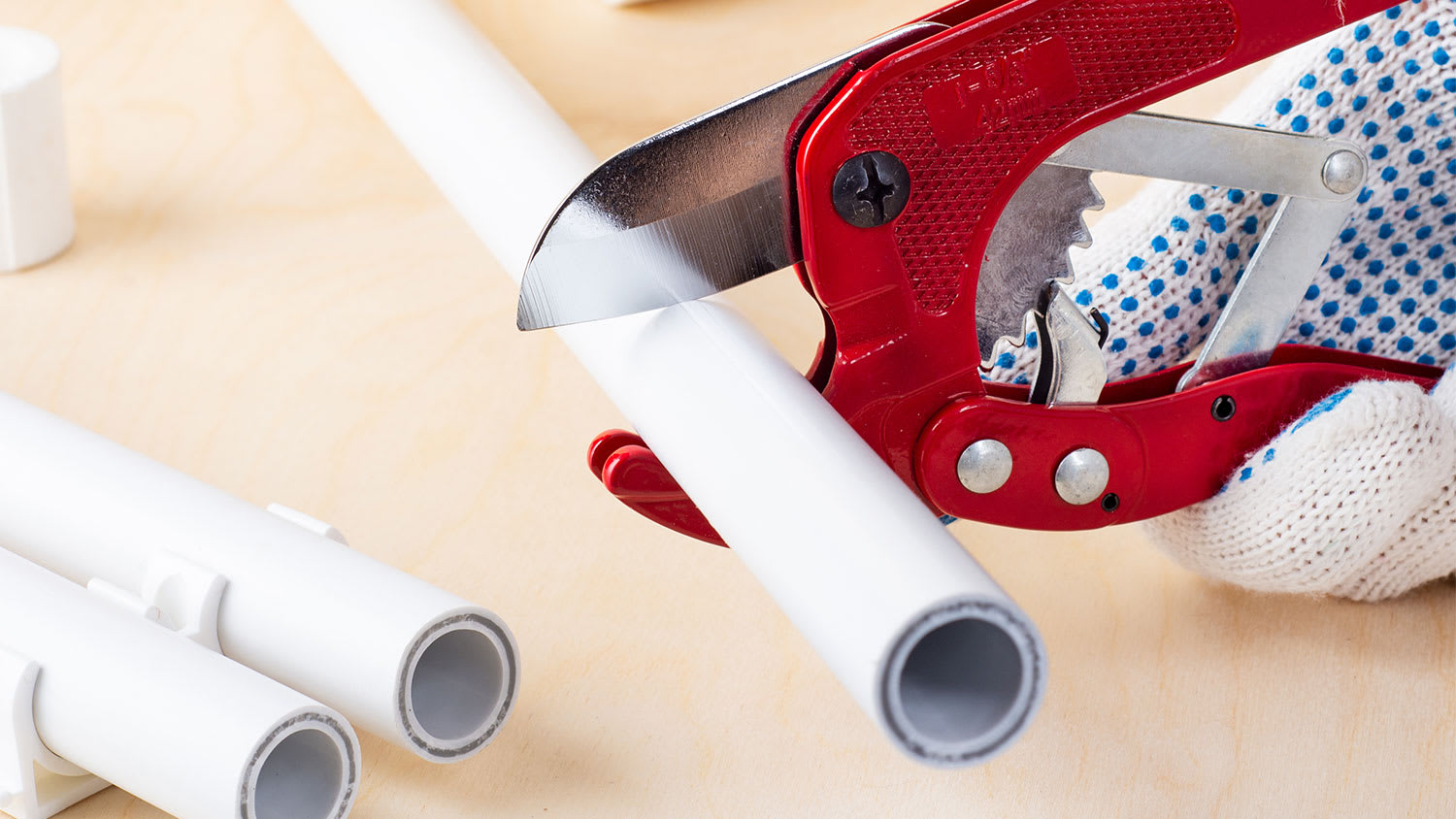 A view of someone using a pipe cutter to cut PVC pipe
