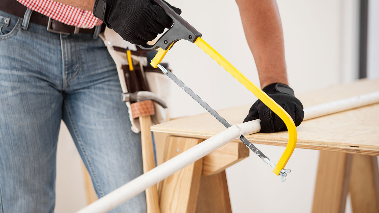 A man uses a hacksaw to cut PVC pipe