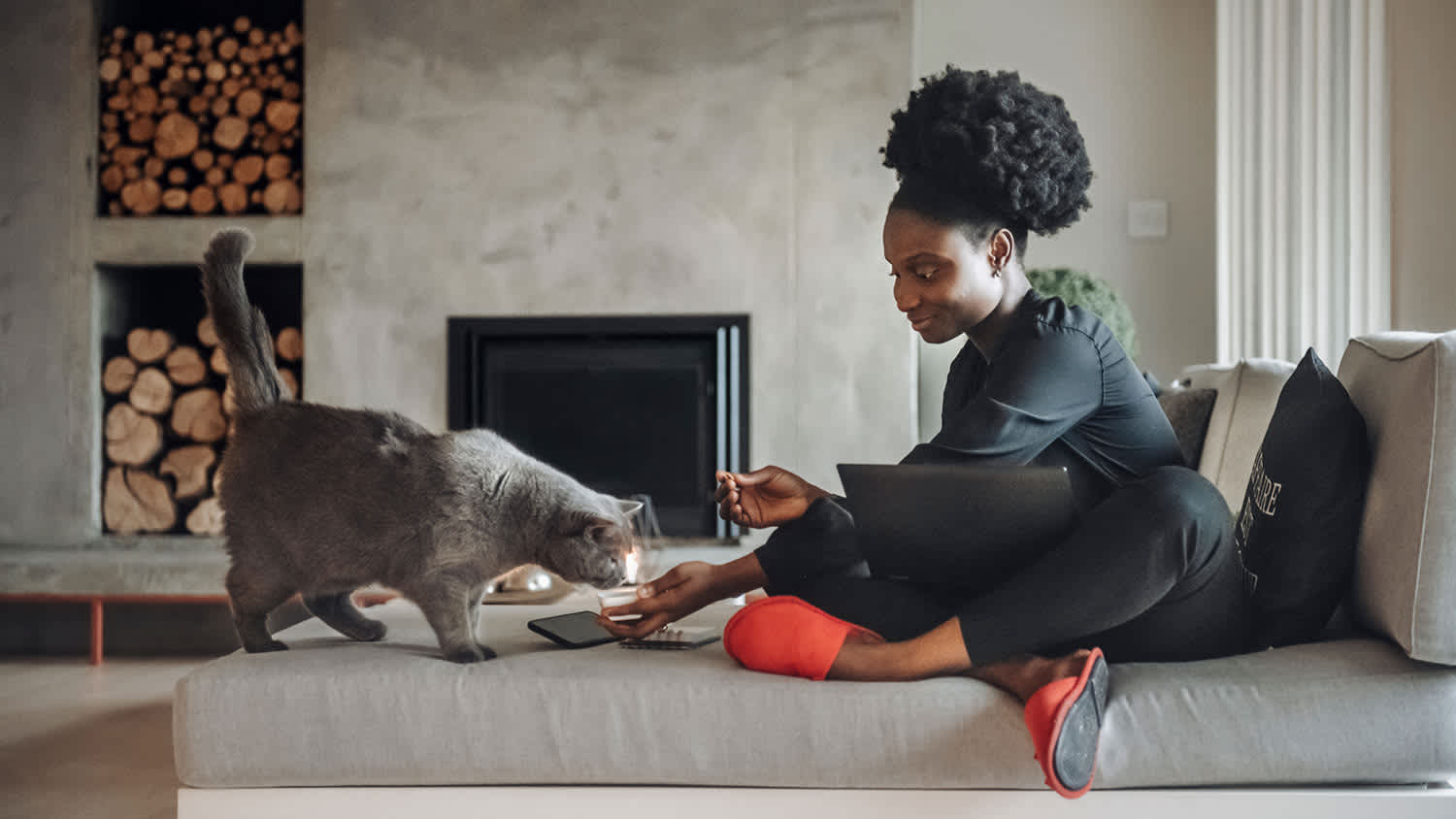 Woman with grey cat on couch in front of fireplace