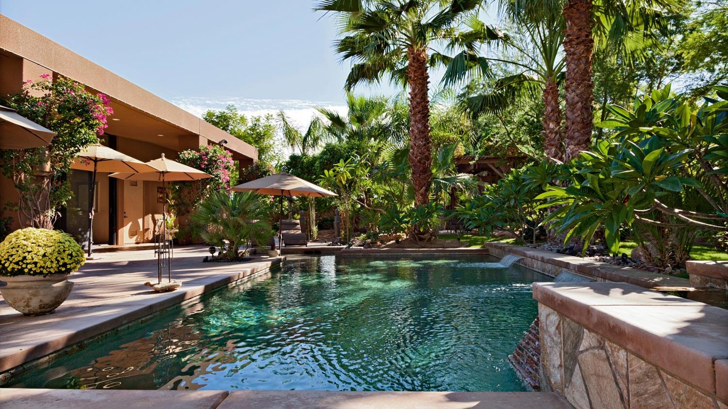 A luxury pool with waterfall and palm trees in the backyard of a villa