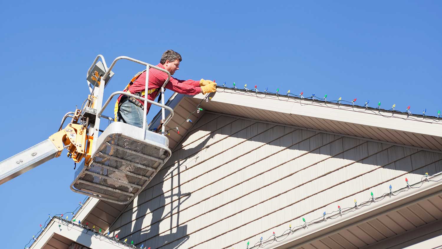 Professional on crane installing Christmas lights on house roof