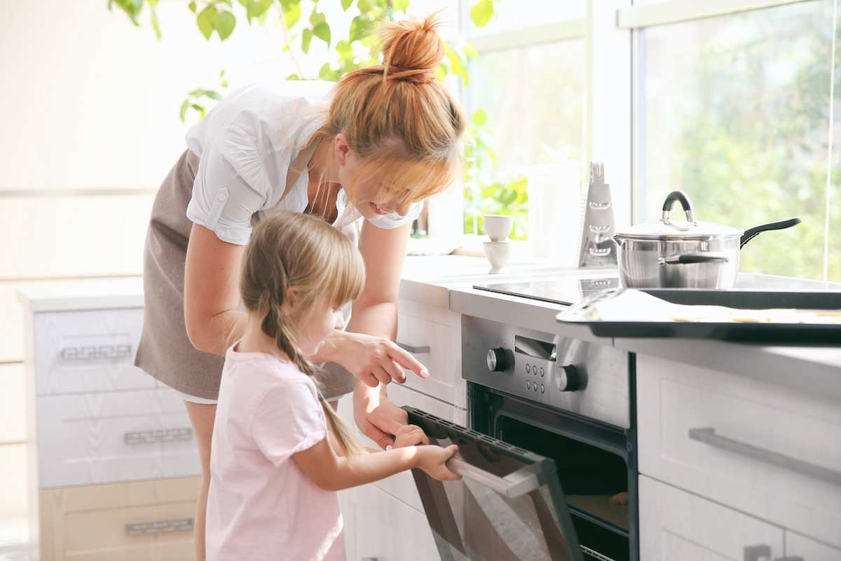 Mother shows daughter how to use the oven in a brightly lit kitchen