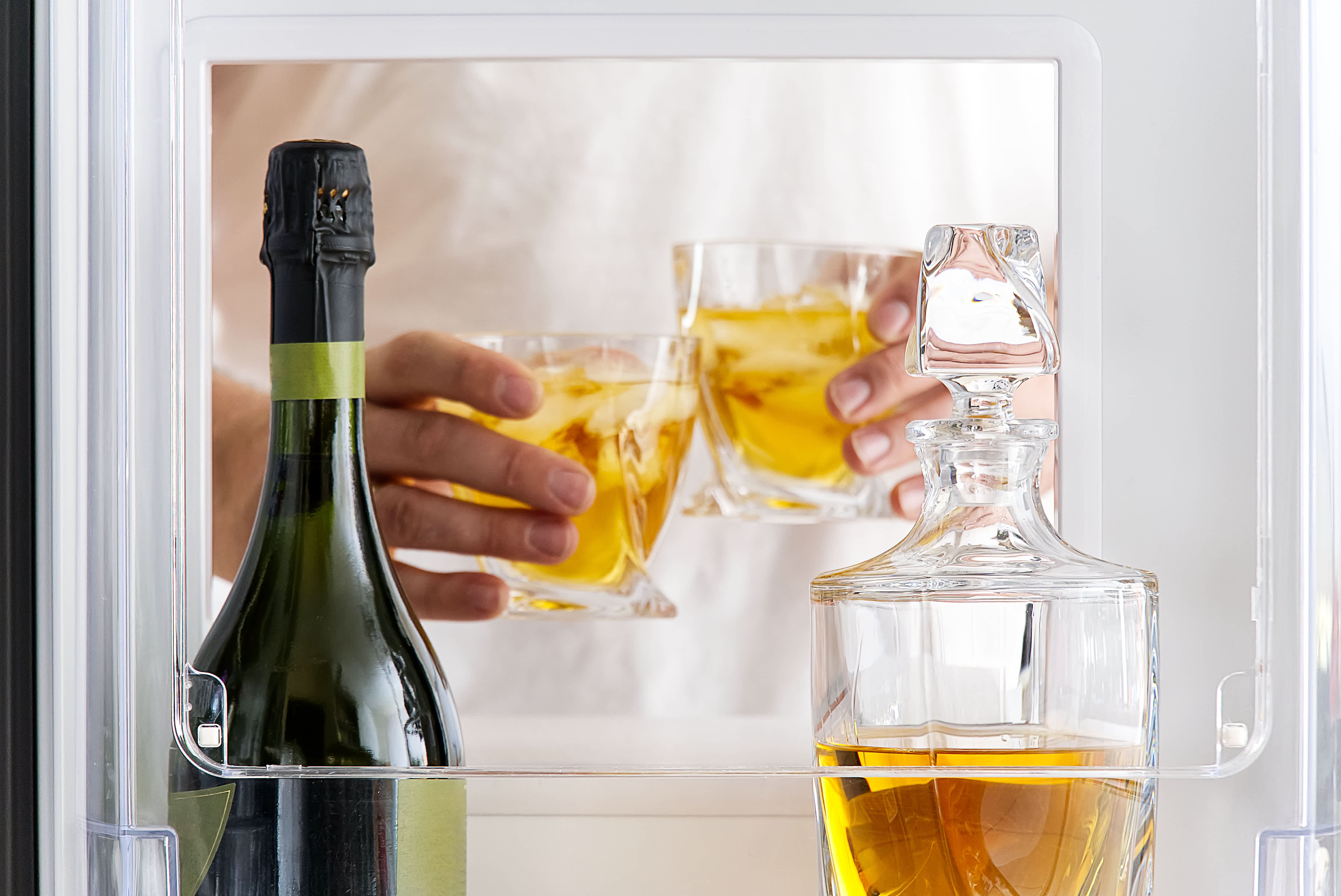 Open hatch mini-fridge with hands toasting, champagne, and a decanter of whiskey