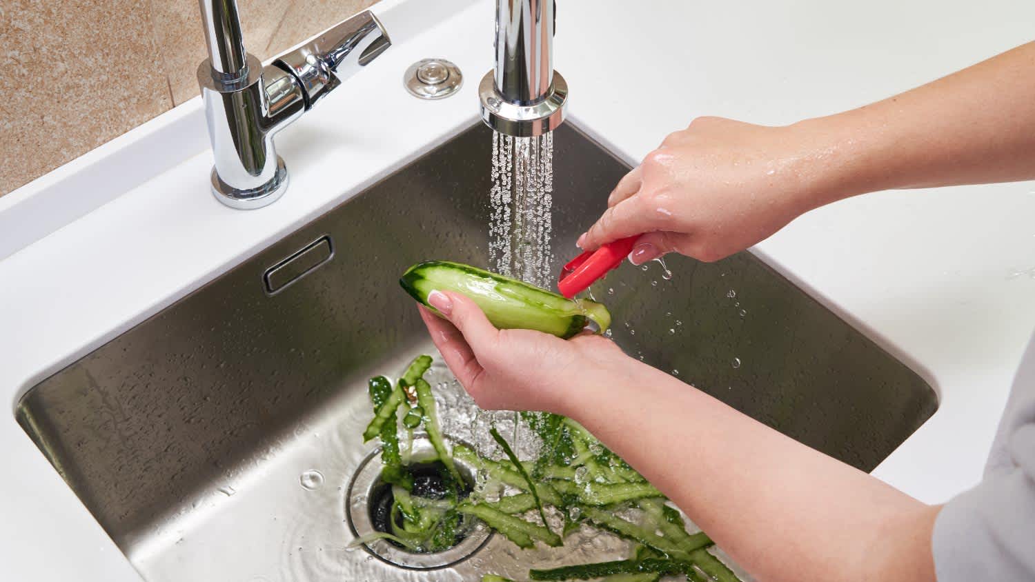 A woman peeling cucumber over Food waste disposer machine