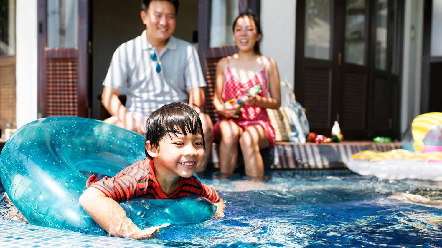 A kid in a swimming pool with his parents overlooking