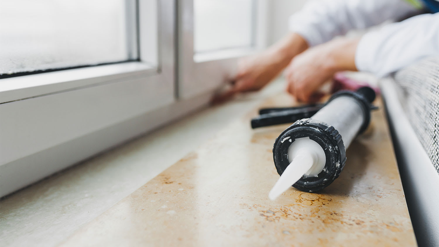 A view of someone caulking a window