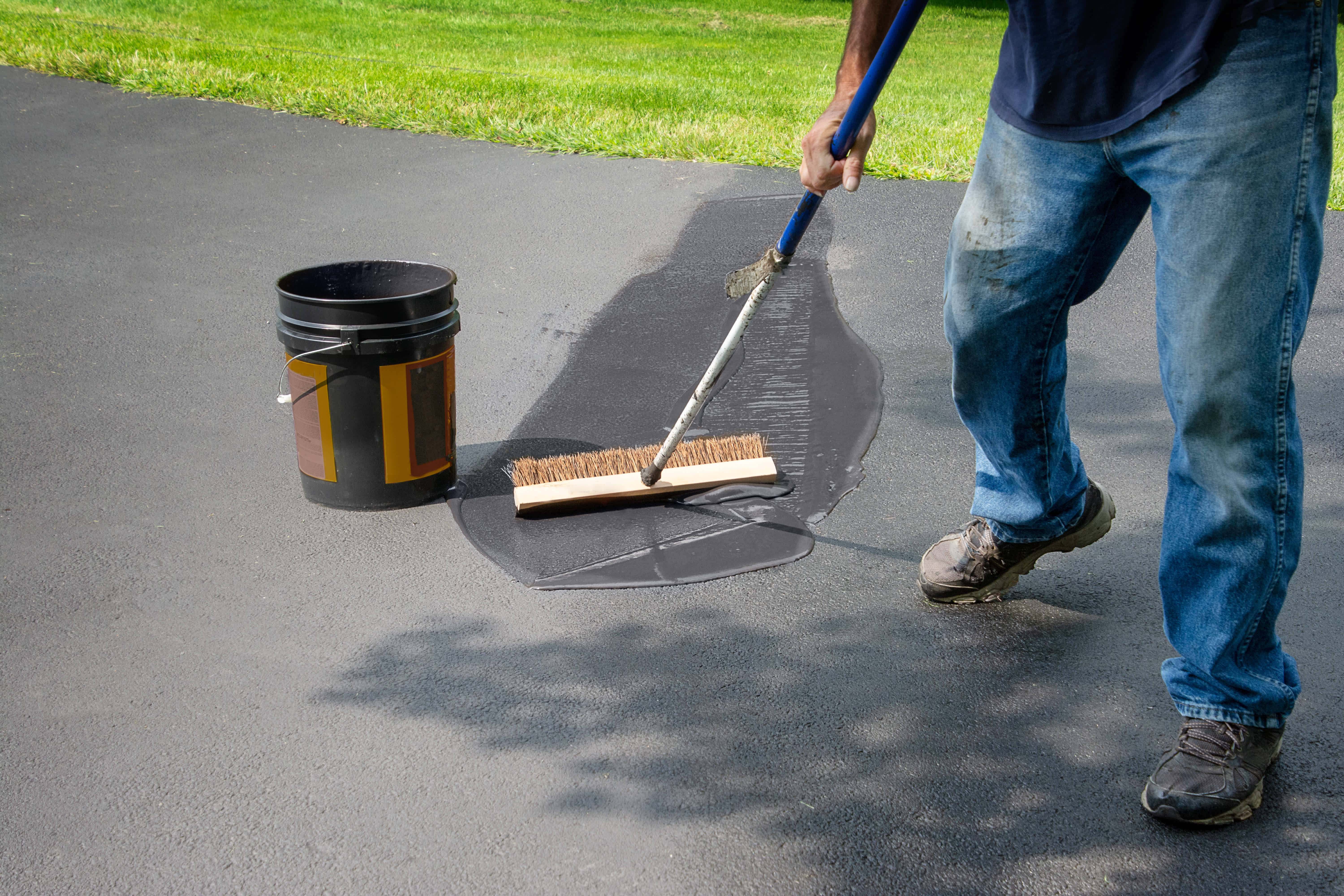 man spreads concrete sealant on driveway