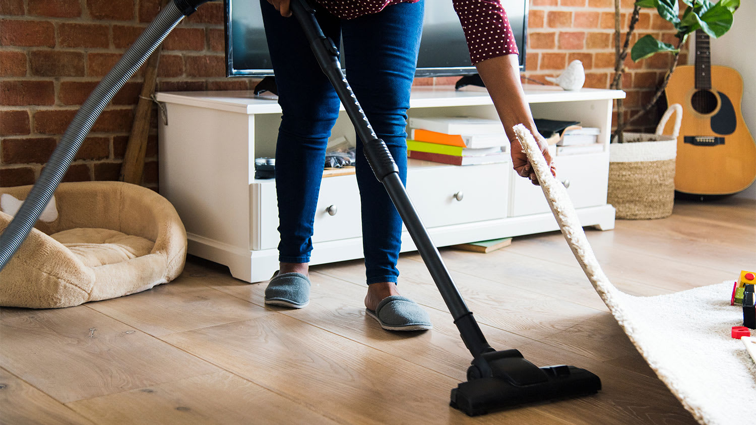 A woman vacuums under a rug