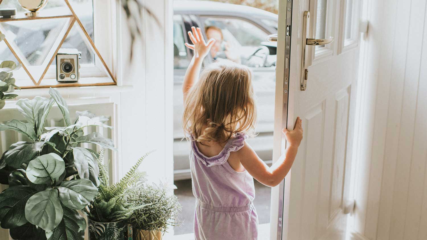 Little girl opening front door and waving