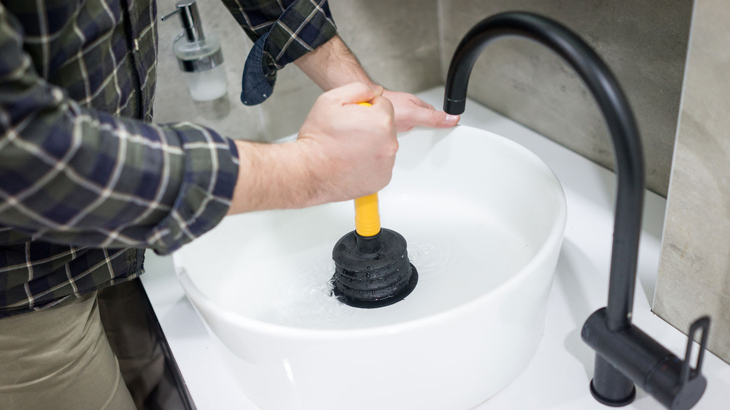 Plumber using plunger in bathroom sink