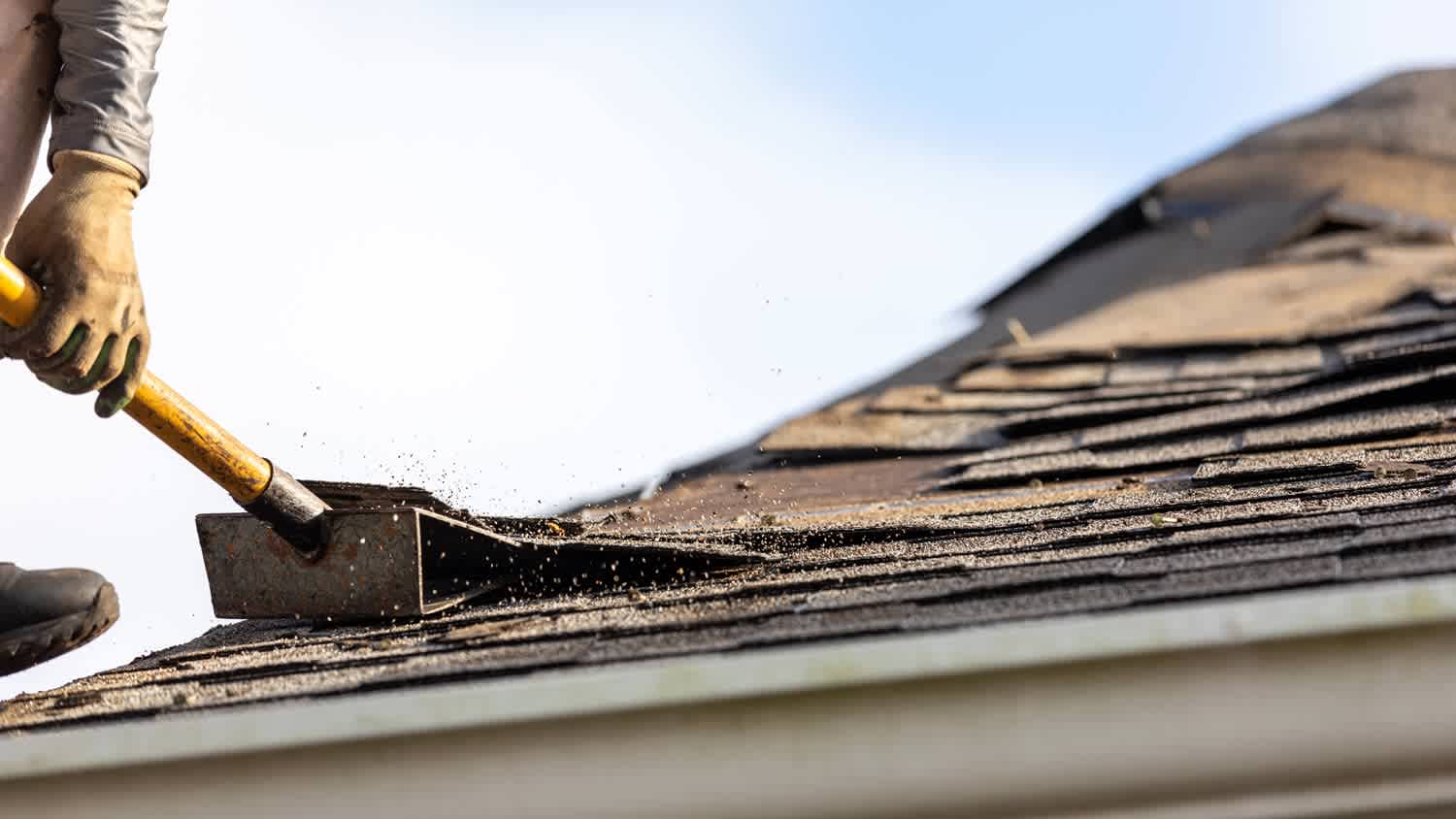 Close-up of a man removing shingles from a roof