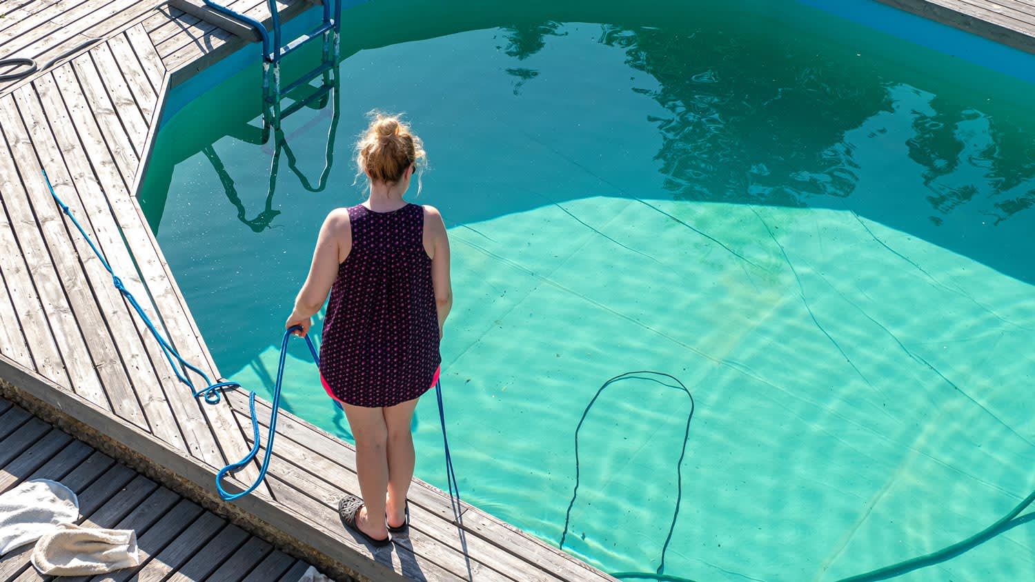 A woman standing on a wooden deck cleaning a swimming pool