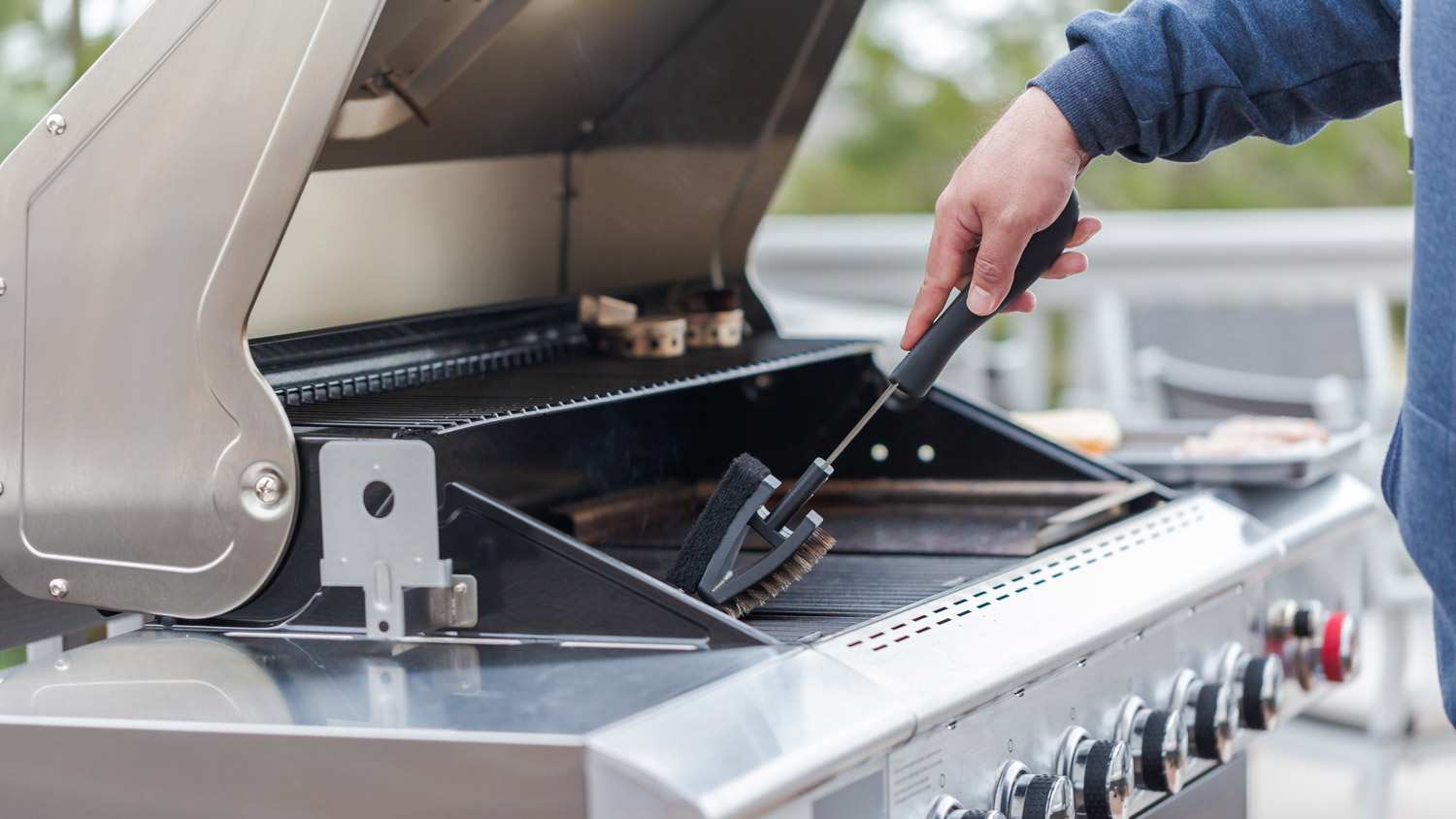 A man cleaning his gas grill using a brush