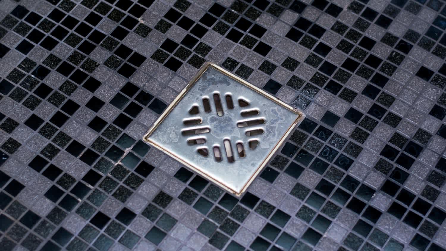 A clean shower drain in a dark gray bathroom