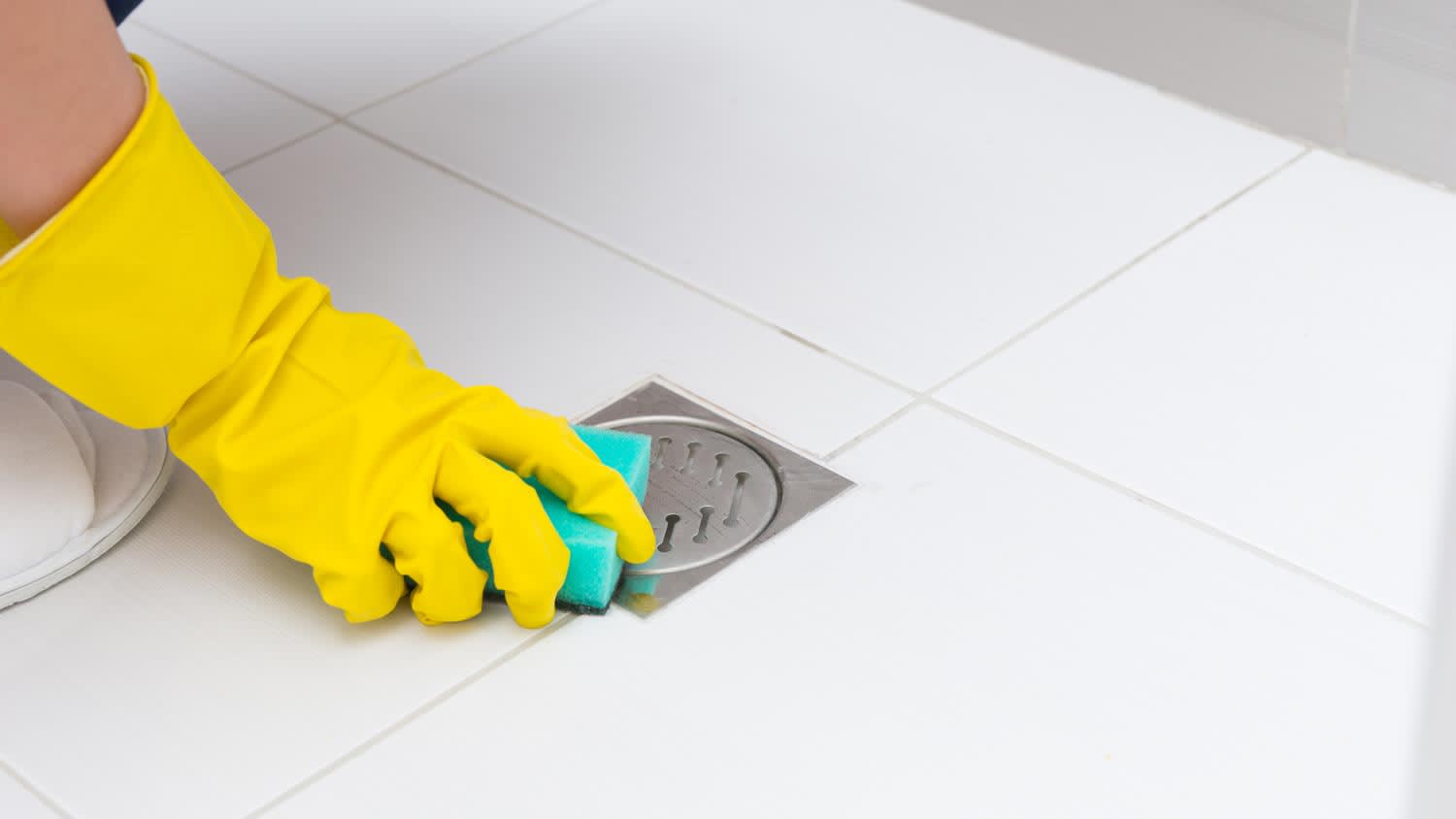 A hand in protective gloves cleaning the shower drain