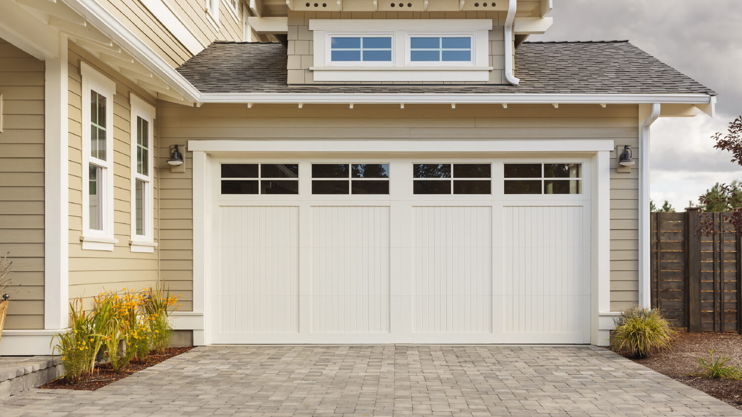 white ranch-style garage door with brick driveway and beige siding