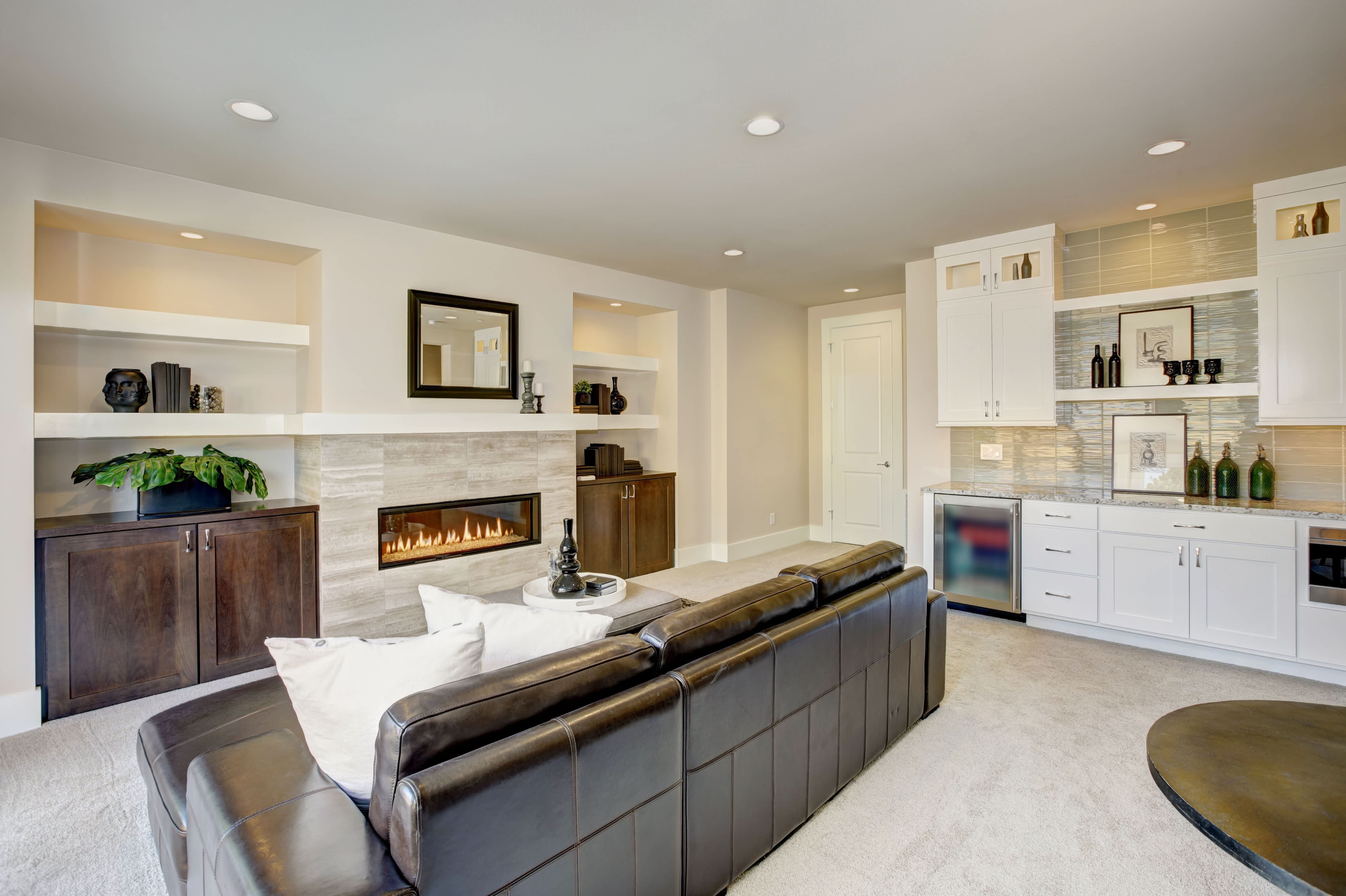 A family room with a wet bar nook, mini-fridge, and white cabinets