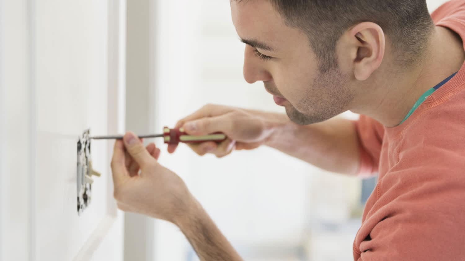A man using a screwdriver replaces a light switch