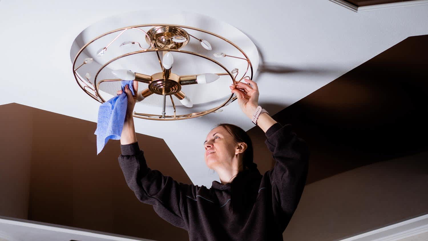 A woman getting rid of cobwebs from a light fixture