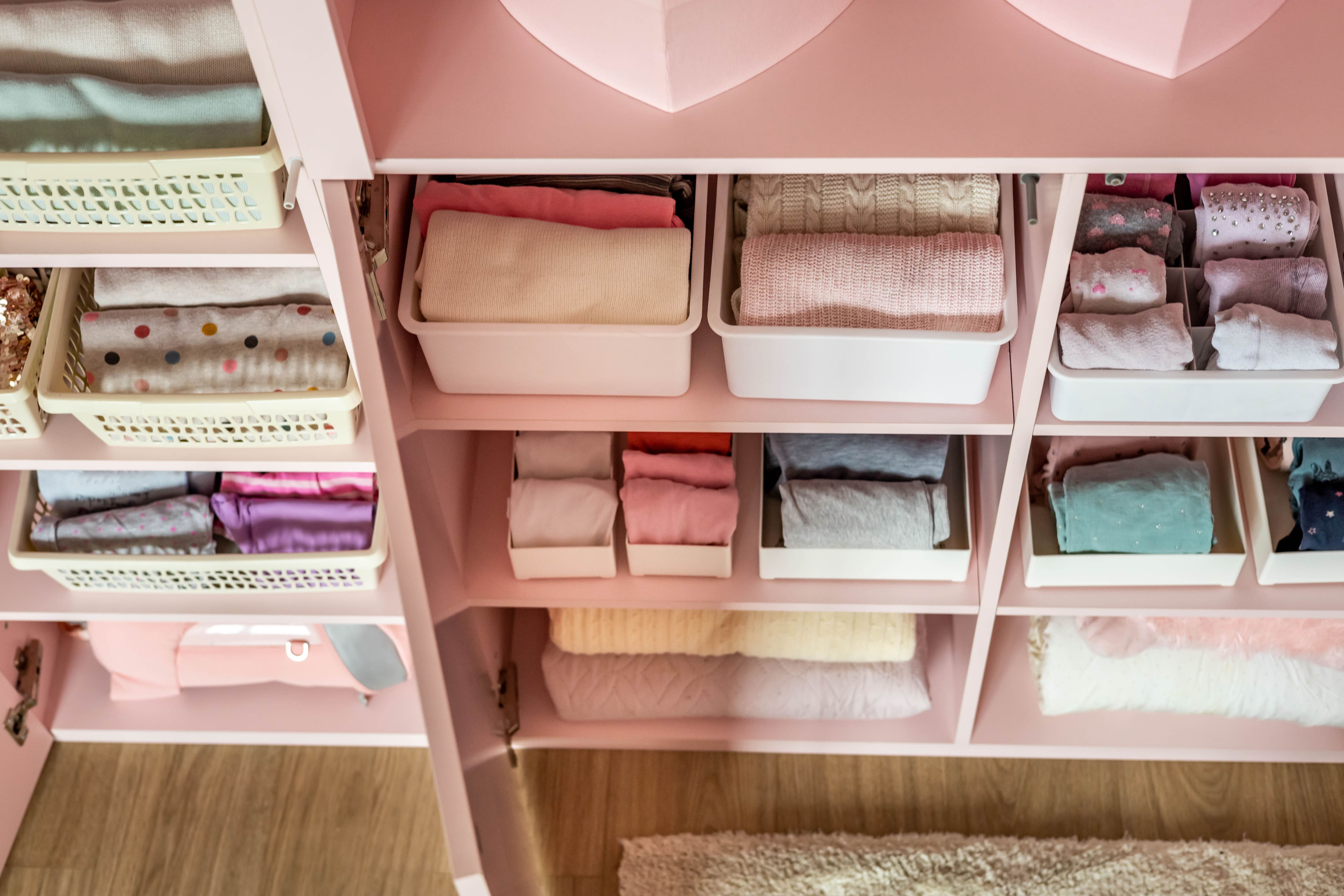 A pink closet with clothes folded in assorted bins and baskets