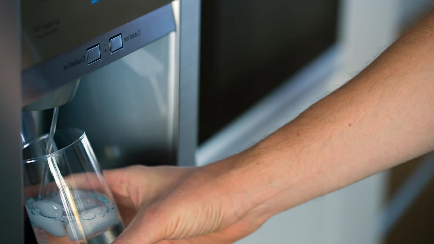 A hand filling a glass with water from the fridge