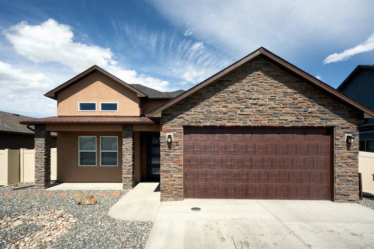 view of brick and brown colored single story home with attached garage and gravel