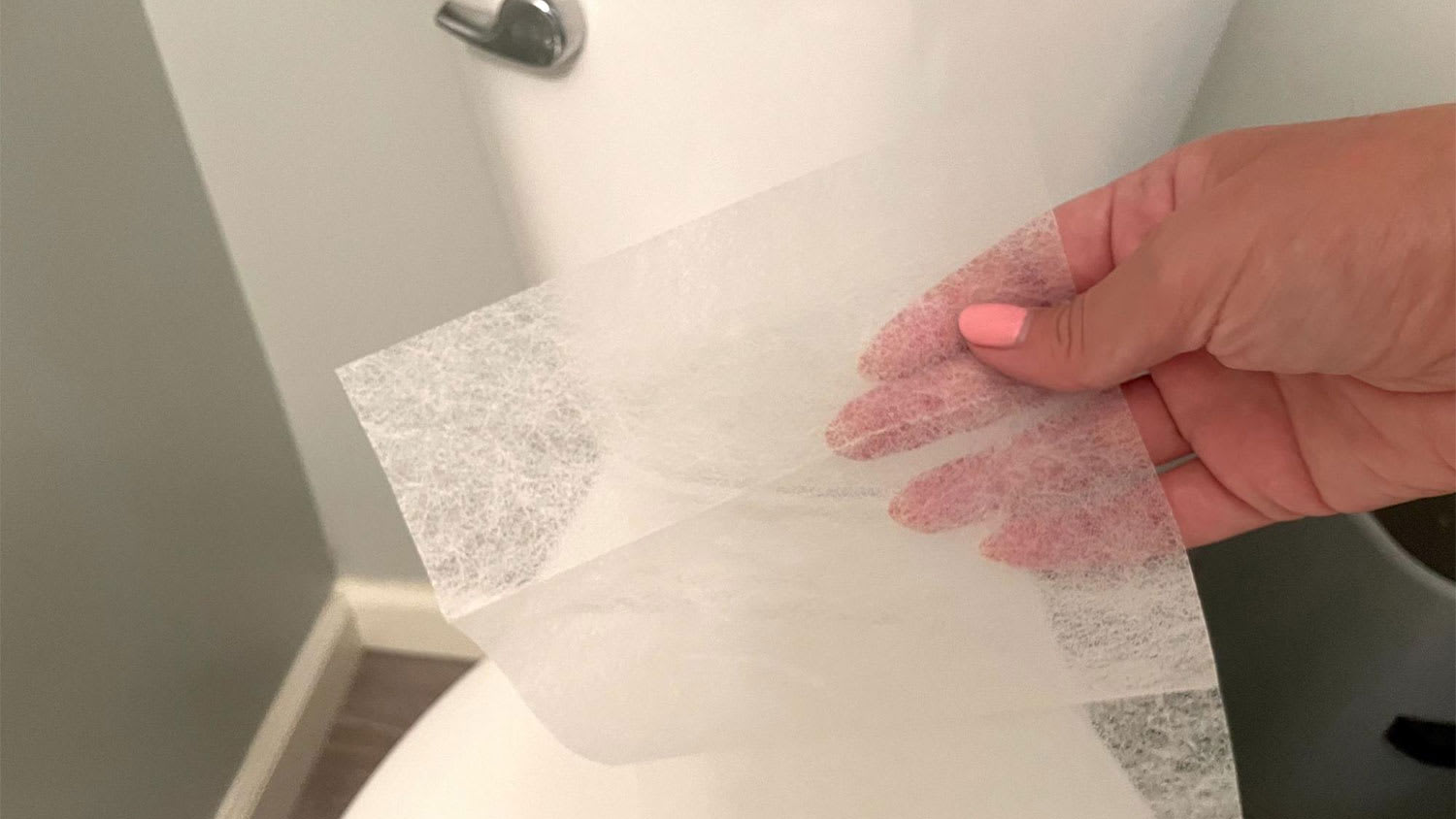 A woman holds a dryer sheet in front of a toilet