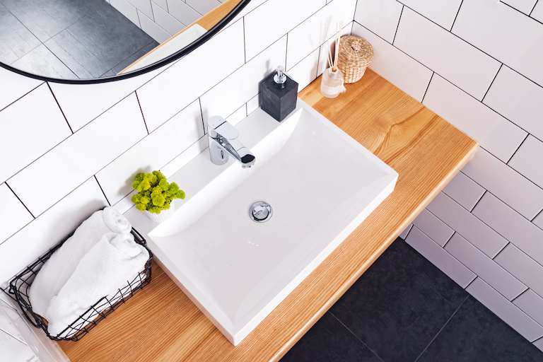 overhead shot of home bathroom interior featuring square sink, light wood counter, and white tile walls