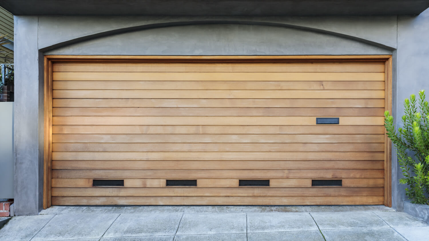 wooden garage door on concrete house with plant