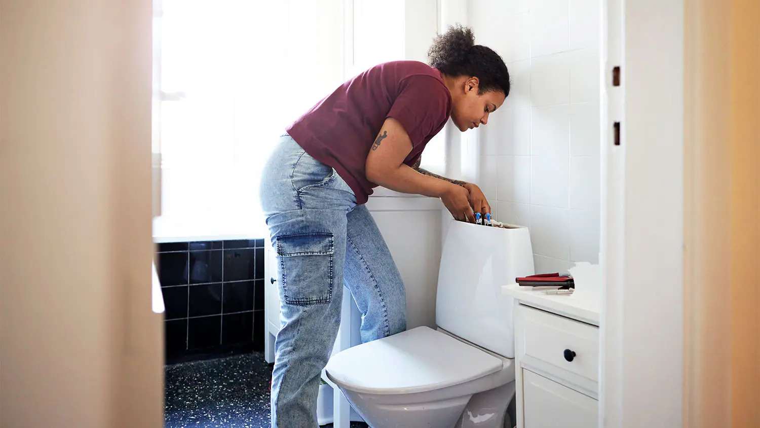 Woman repairing toilet in home bathroom
