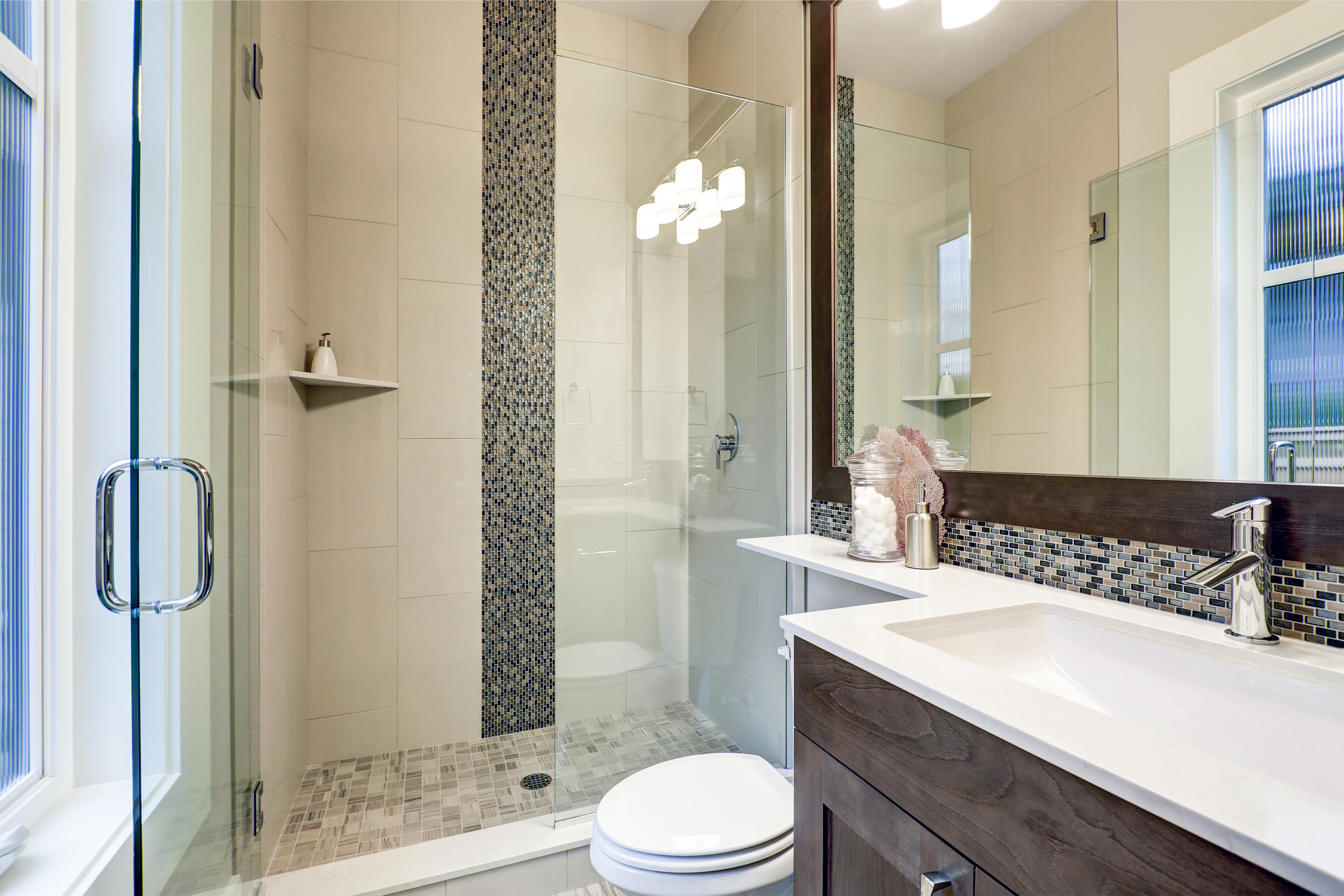 A walk-in shower with a vertical mosaic stripe and matching vanity tile